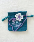 Gehäkelte Blume mit violetter Kordel auf blauem Stoff-Säckchen mit Spiralmotiv auf leinentuch Hintergrund