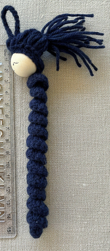 Blaues handgehäkeltes Sorgenwürmchen als Anhänger neben Lineal zur Größenveranschaulichung