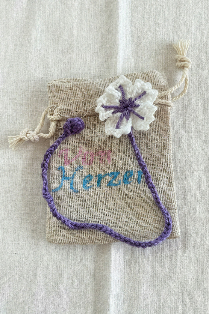 Handgemachtes gehäkeltes Lesezeichen mit lila Herz und kleiner Blume in einem Stoffbeutel