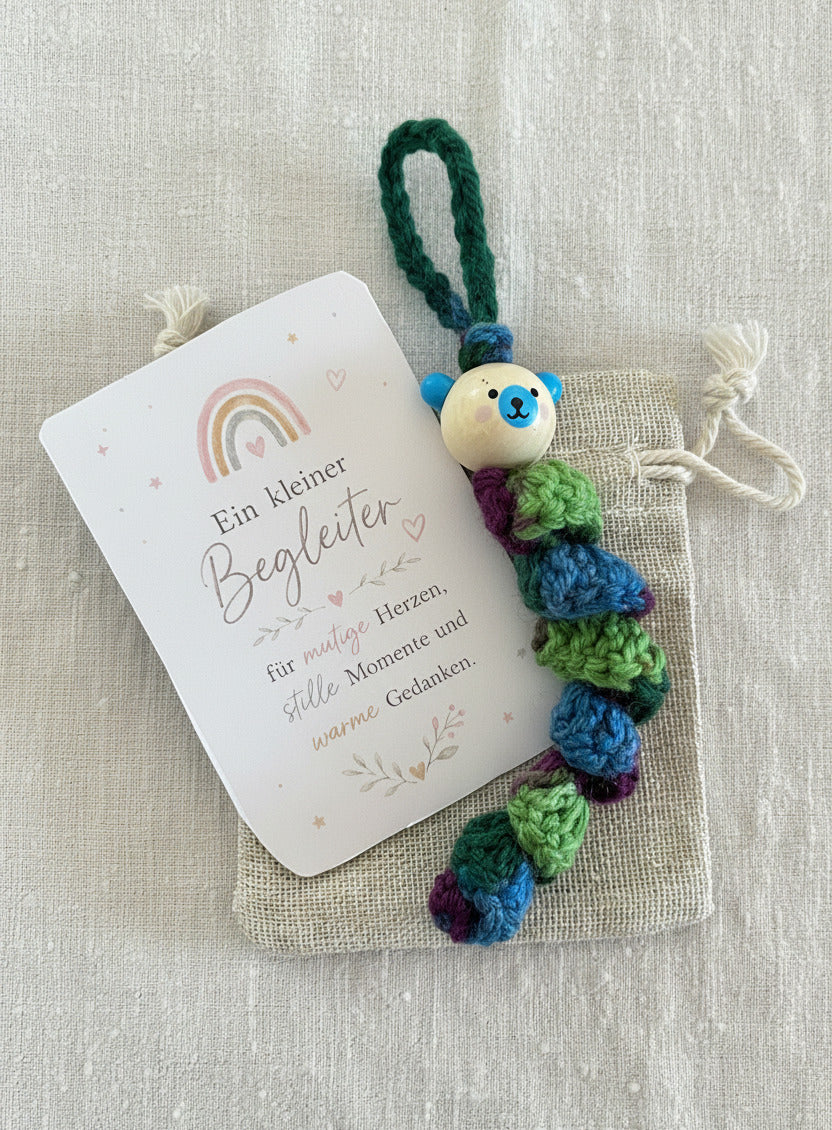 Handgemachtes Sorgenbärchen in Regenbogenfarben mit Stoffbeutel und Karte „Ein kleiner Begleiter“ auf hellem Hintergrund 🌈🧸💚