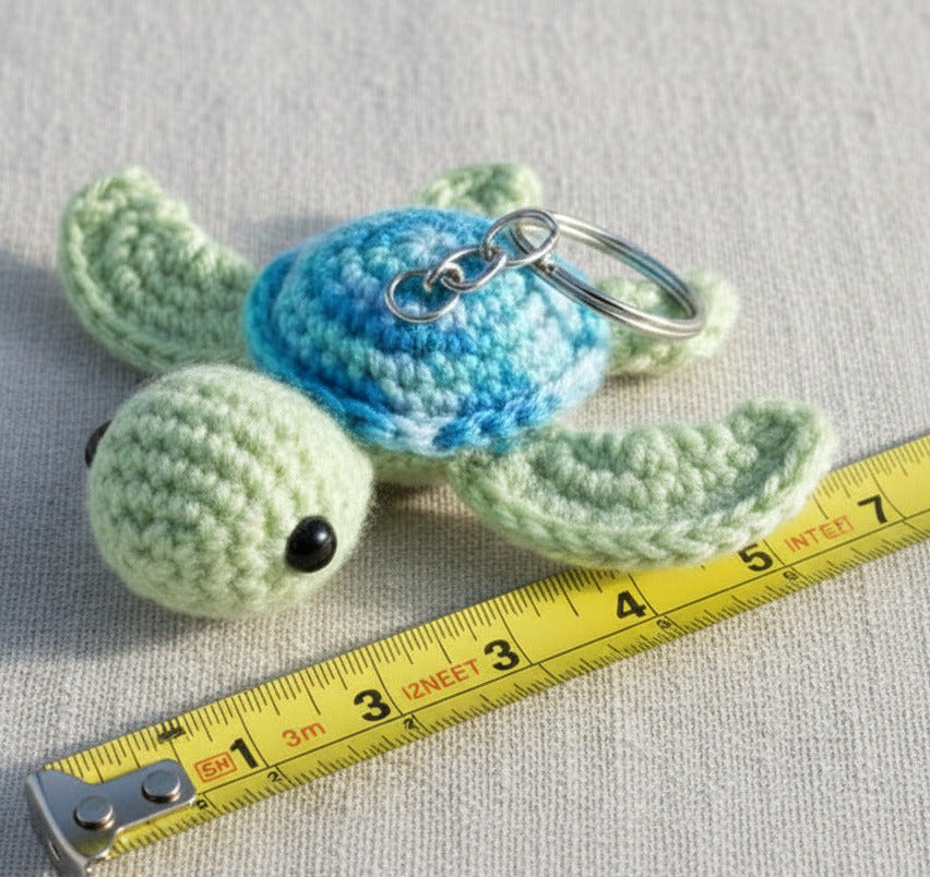 Gehäkelte Schildkröte Schlüsselanhänger in Blau und Grün mit Maßband als Größenvergleich, handgemacht im Amigurumi Stil
