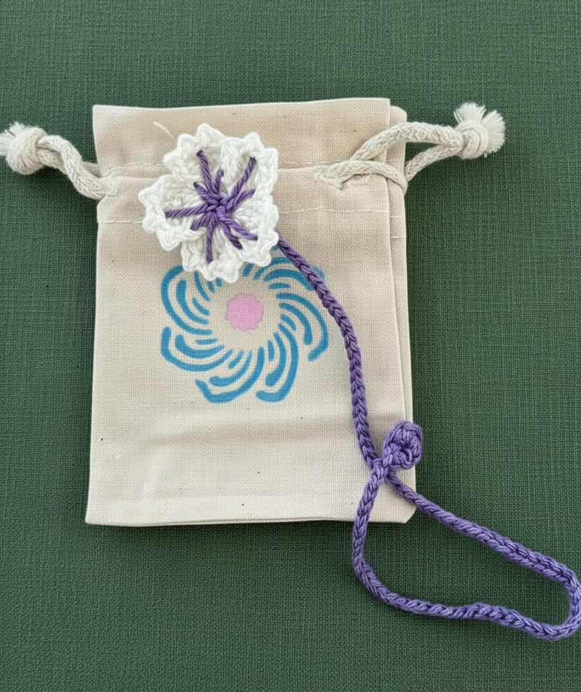 Handgemachtes gehäkeltes Lesezeichen mit Blume und Stoff-Säckchen auf hellem Hintergrund.
