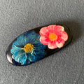 Handbemalter Glücksstein mit blauer und rosa Blüte auf schwarzem Naturstein. Liebevoll gestaltetes Unikat als Geschenk und Dekoration.
