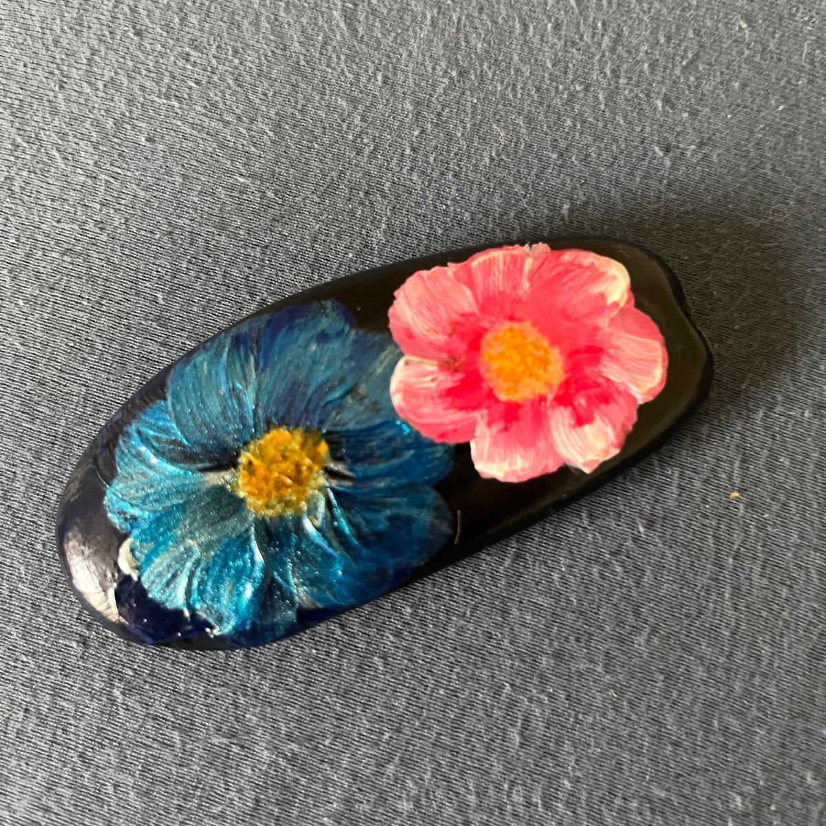 Handbemalter Glücksstein mit blauer und rosa Blüte auf schwarzem Naturstein. Liebevoll gestaltetes Unikat als Geschenk und Dekoration.