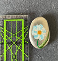 Handbemalter Glücksstein mit weiß-blauem Blumenmotiv auf ovalem Naturstein. Liebevoll gestaltetes Unikat als Glücksbringer und Geschenkidee.