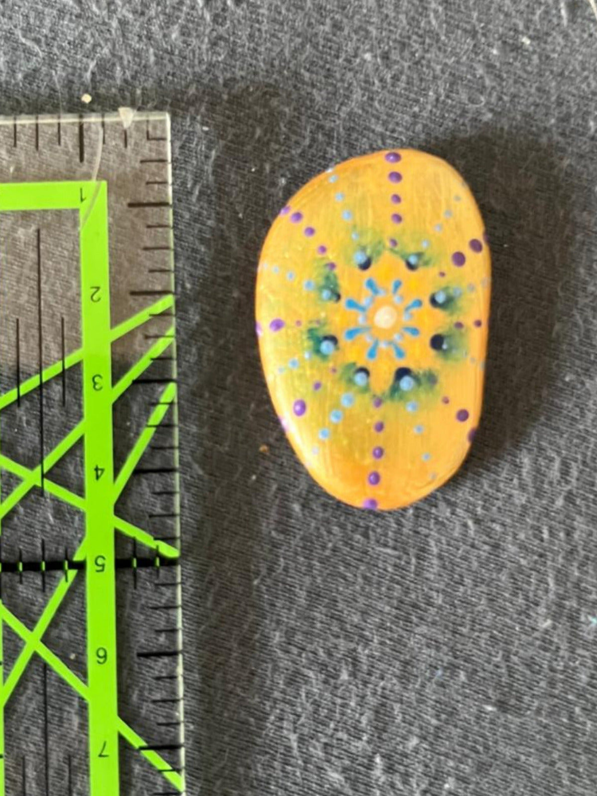 Handbemalter Glücksstein mit Mandala-Blütenmuster in Blau, Grün, Weiß und Violett auf warmgelbem Stein. Liebevoll gestalteter Glücksbringer im Taschenformat