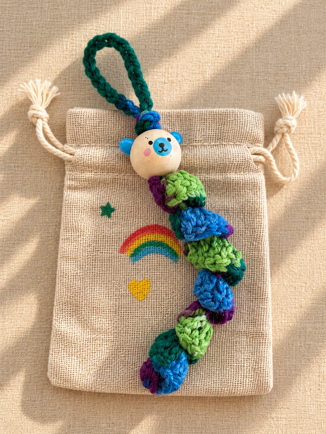 Handgemachte bunte Häkelraupe mit bemaltem Holzperlenkopf und Stoff-Säckchen mit Regenbogen