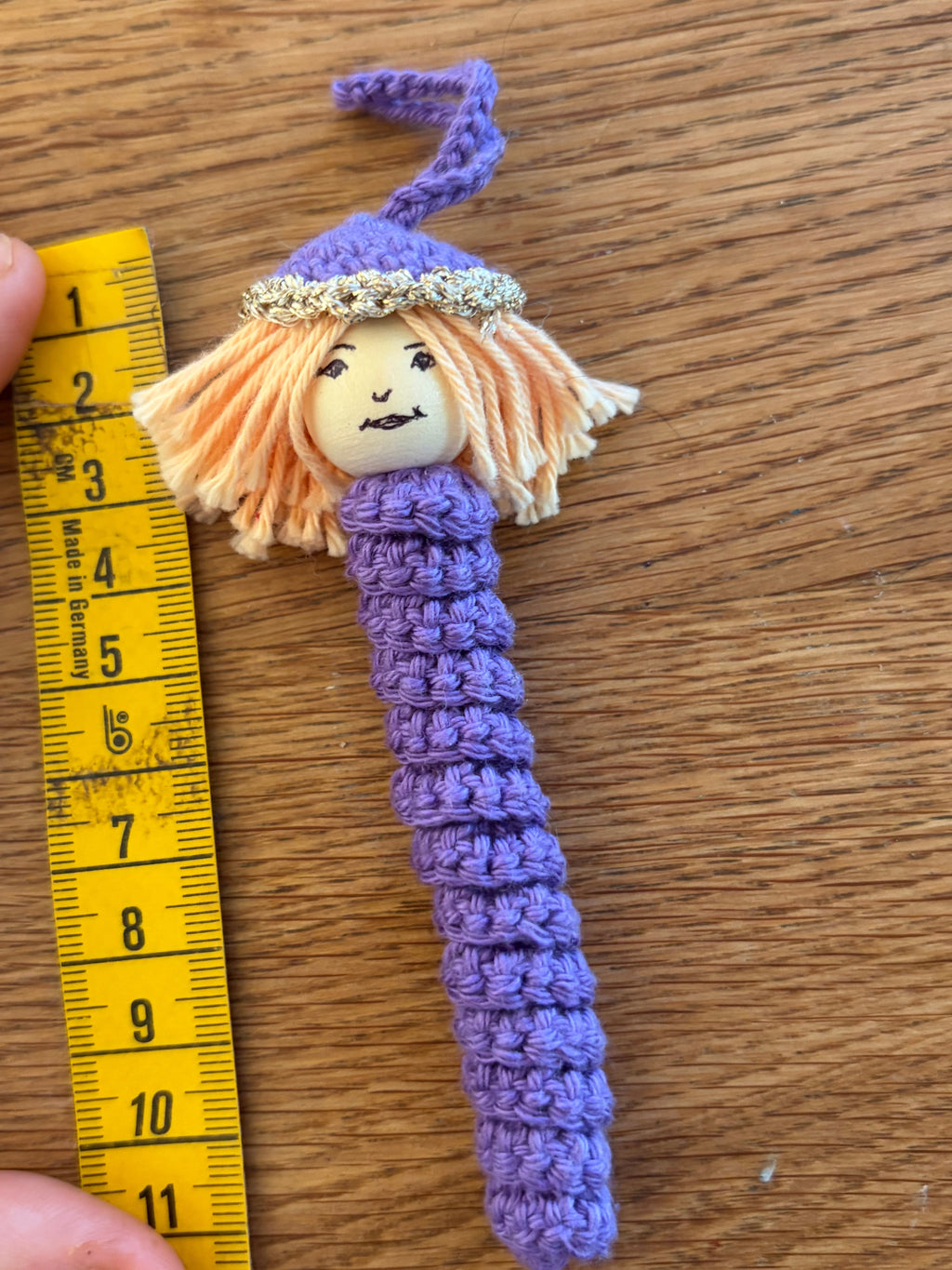 Lila handgehäkeltes Sorgenmädel neben einem Massband zur Grössenbestimmung. Liebevoll gefertigter Mutmacher und Trostspender für Kinder.