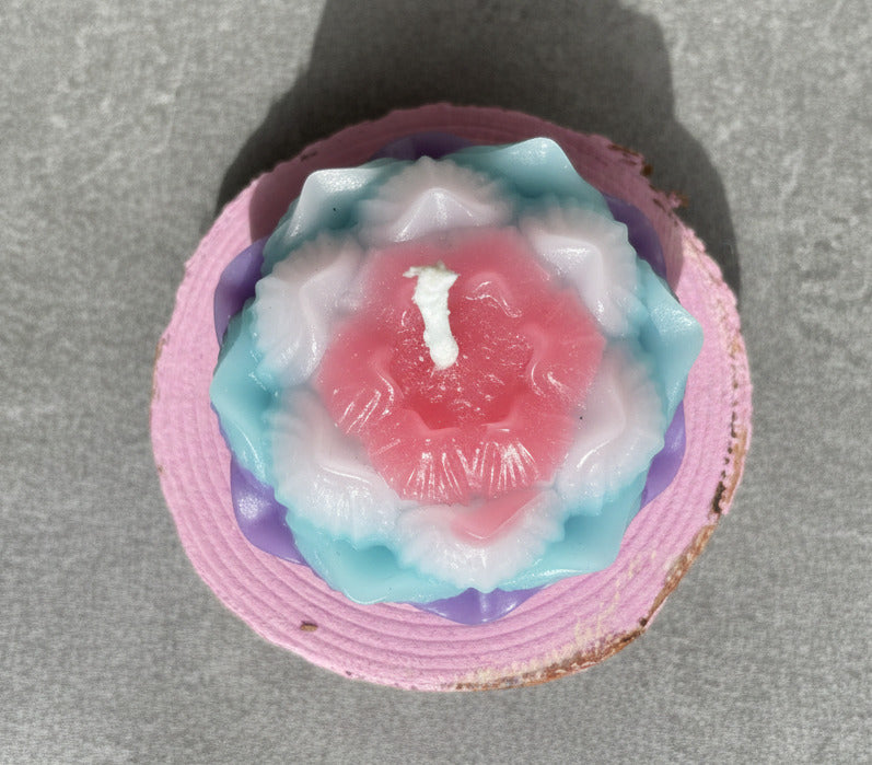 Lotusblüten Kerze in Blau, Rosa und Weiß von oben auf Holzscheibe
