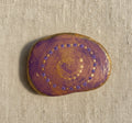 Handbemalter Mandala-Spirale-Stein in Lila und Gold mit feinen Punktmustern auf hellem Hintergrund
