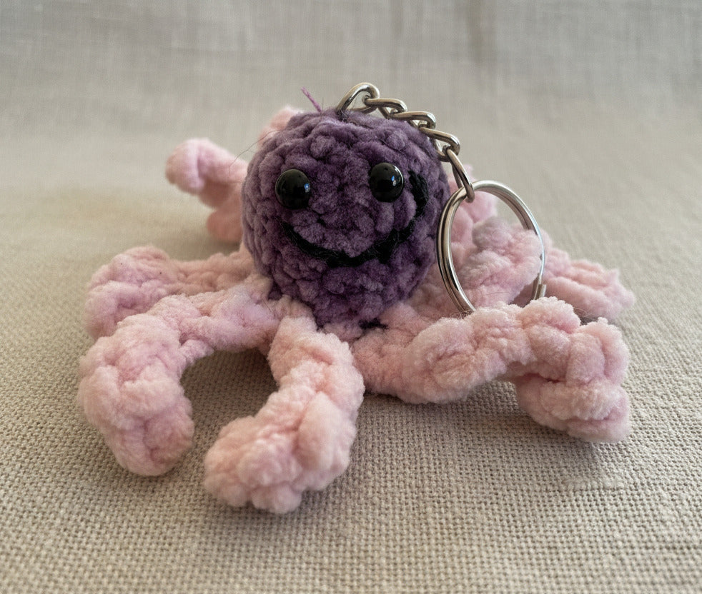 Detailaufnahme eines gehäkelten Tintenfisch Schlüsselanhängers in rosa und lila mit Gesicht und Metallring, handgemacht