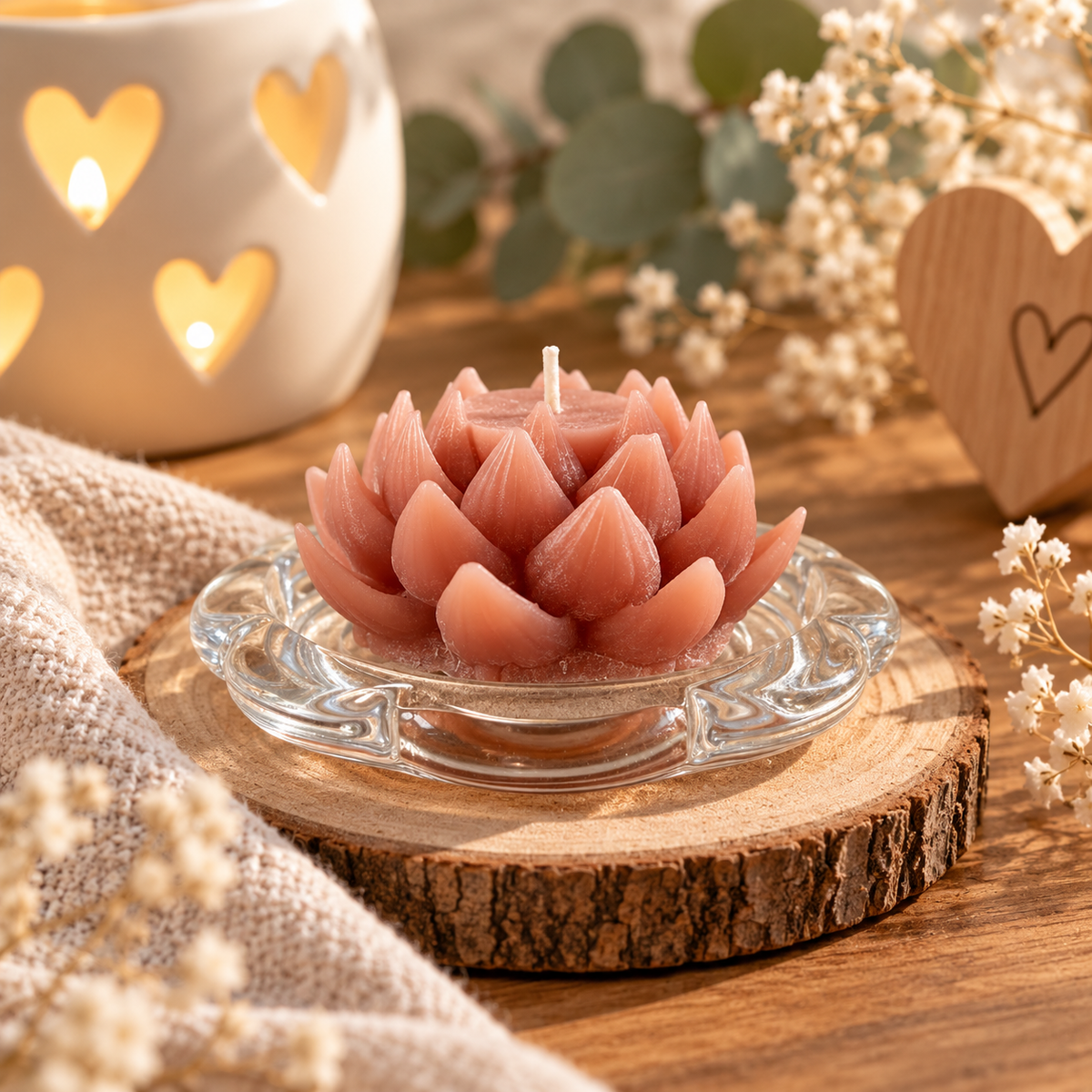 Handgemachte rosa Lotuskerze auf Glasteller in warmer, gemütlicher Dekoration mit Trockenblumen und Holzherz.