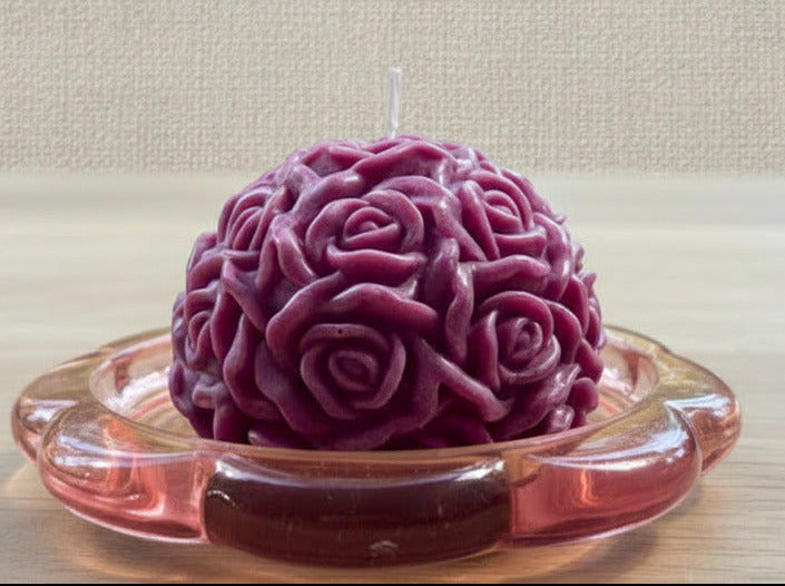 Violette handgegossene Rosenkerze in Kugelform auf rosa Glasteller – dekorative Kerze aus Wachs