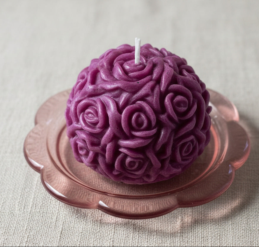 Violette handgegossene Rosenkerze in Kugelform auf rosa Glasteller – dekorative Kerze aus Wachs