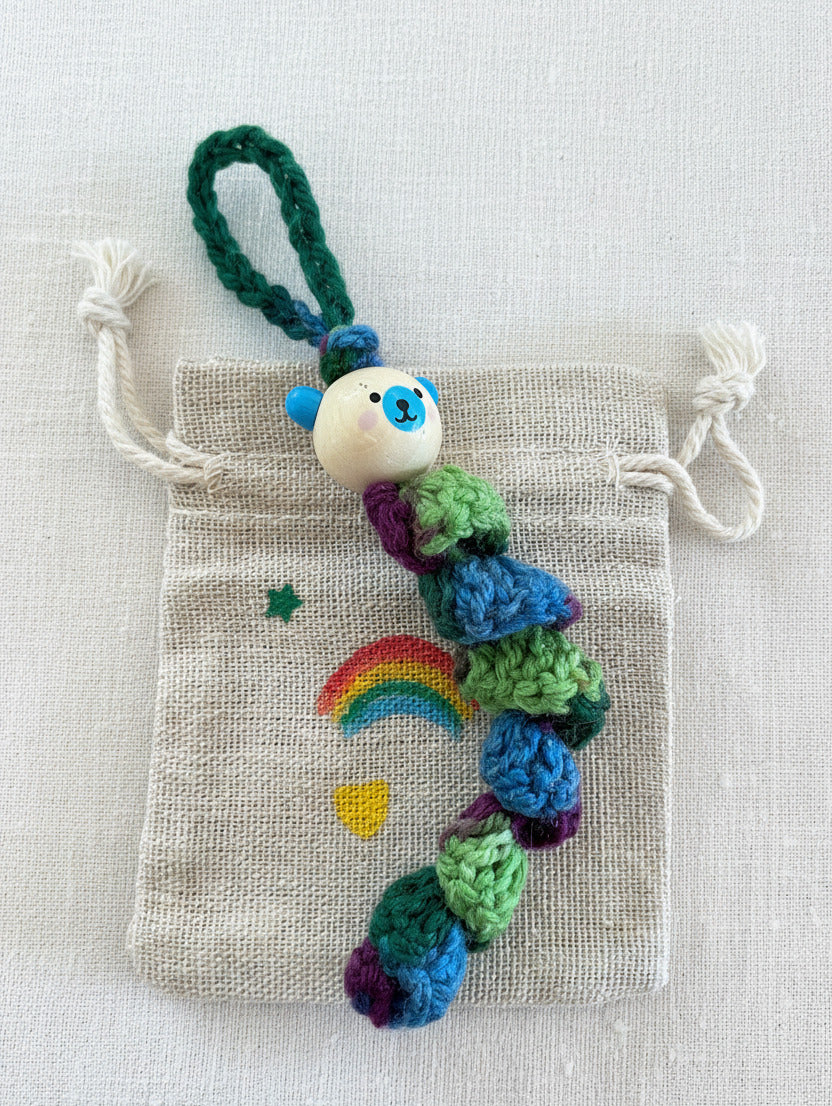 Handgemachtes Sorgenbärchen in Regenbogenfarben mit Stoffbeutel und kleinem Regenbogen auf Holzuntergrund 🌈🧸