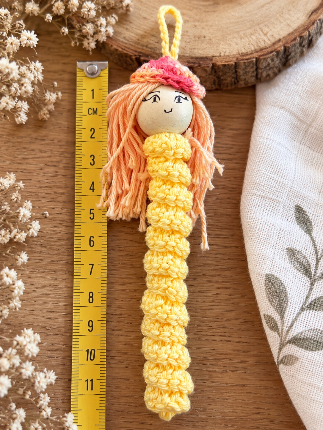 Gelbes gehäkeltes Sorgenmädchen mit orangefarbenen Haaren und Mütze neben einem Lineal zur Darstellung der Größe.