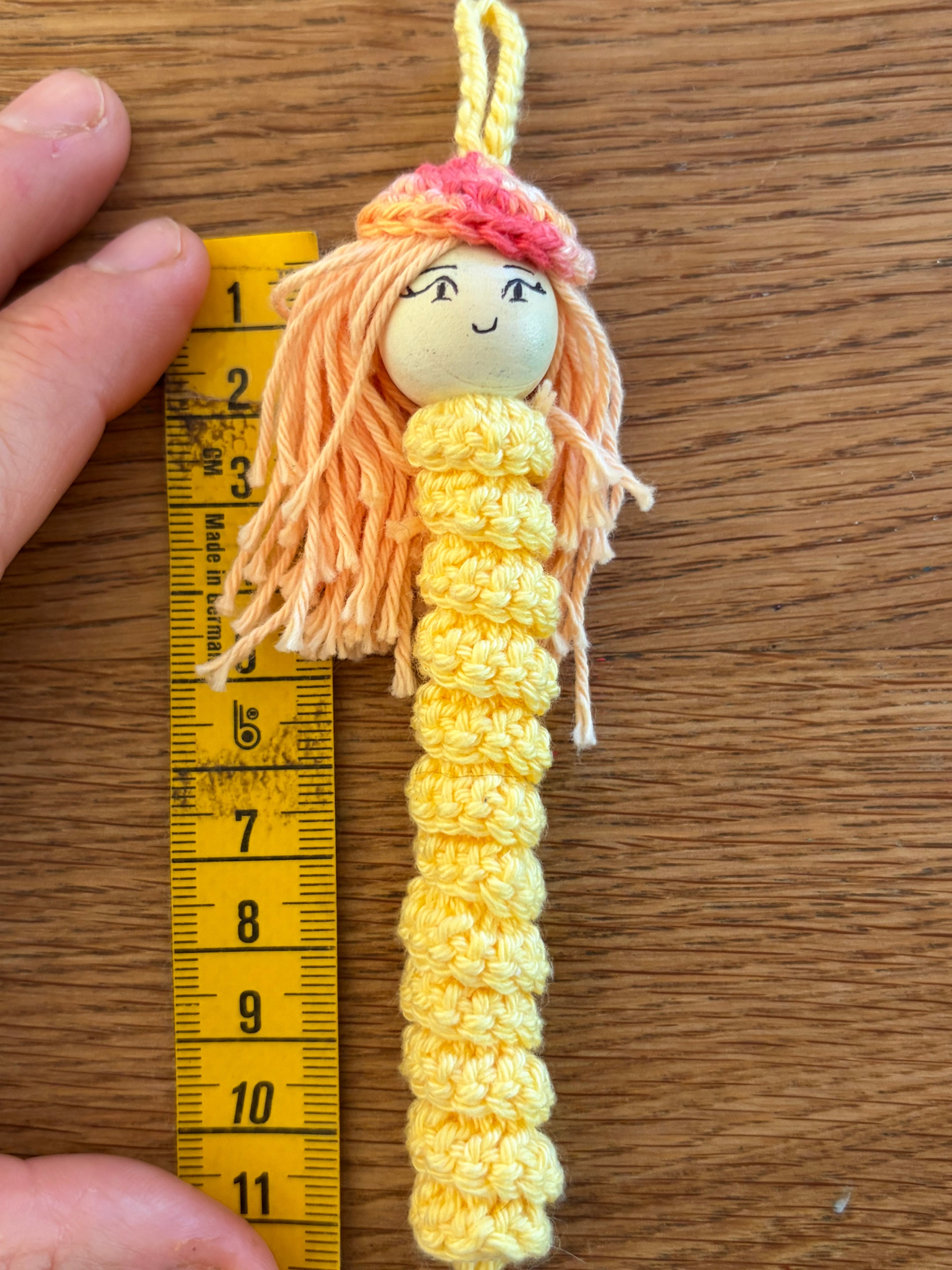 Gelbes handgehäkeltes Sorgenmädel neben einem Massband zur Darstellung der Grösse. Liebevoll gefertigter Mutmacher für Kinder.