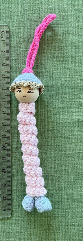Handgehäkeltes Sorgenwürmchen als Anhänger in Rosa mit kleiner Puppe neben Lineal zur Größenveranschaulichung