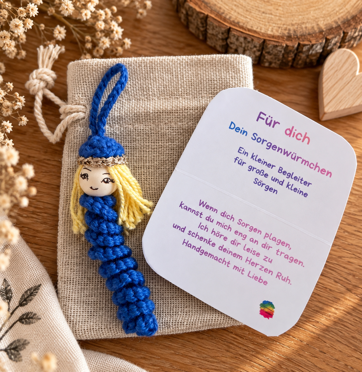 Blaues gehäkeltes Sorgenwürmchen mit blonden Haaren, Spruchkarte und Leinensäckchen als kleines handgemachtes Geschenk.