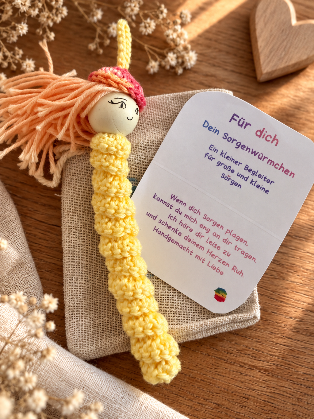 Gelbes gehäkeltes Sorgenwürmchen mit Karte und Leinensäckchen als liebevolles kleines Geschenk.
