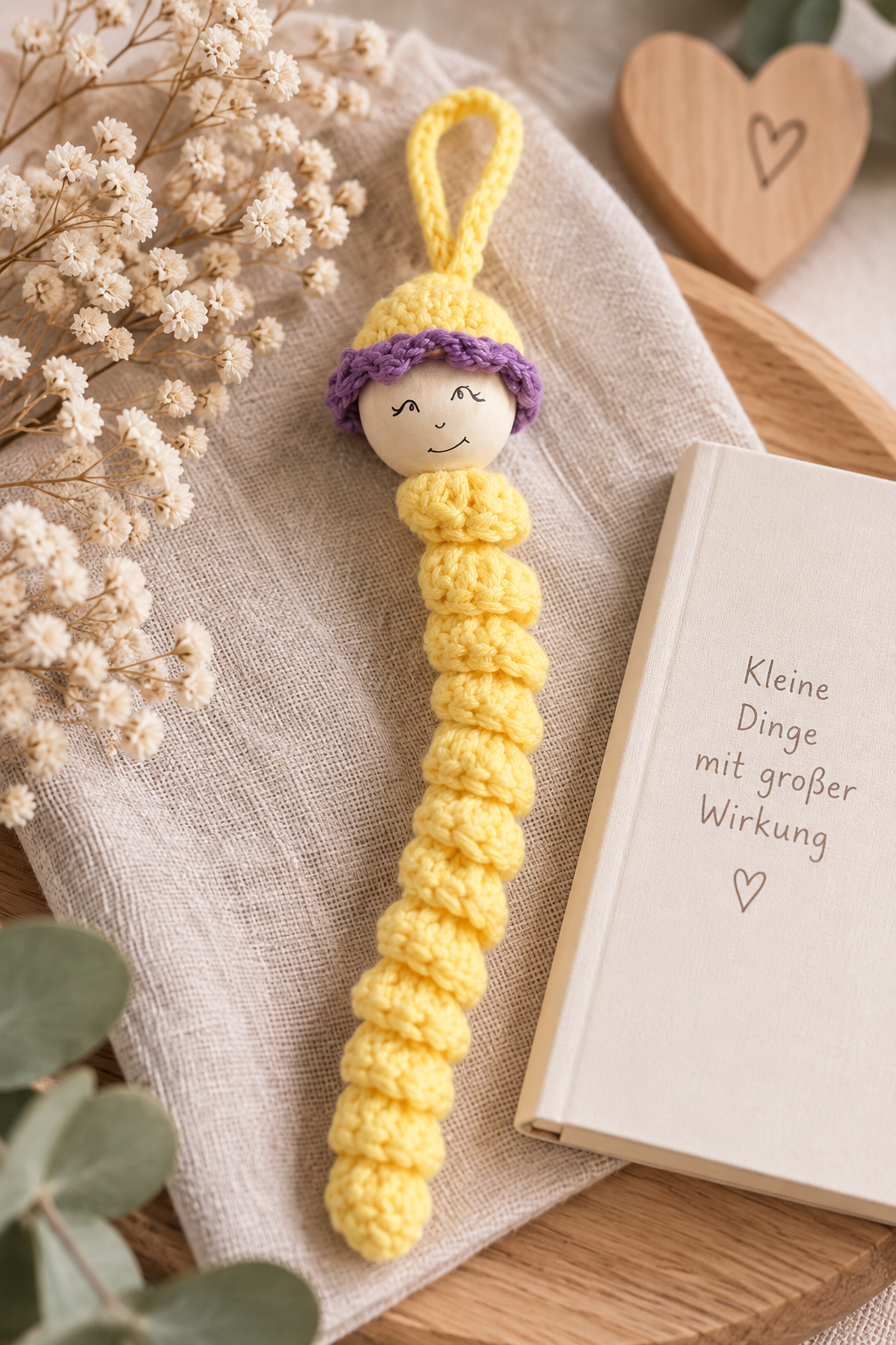 Handgehäkeltes gelbes Sorgenwürmchen mit violetter Mütze in liebevoller Geschenkdekoration.
