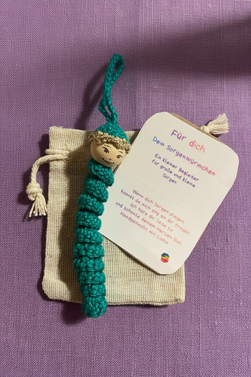 Handgehäkeltes Sorgenwürmchen als Glücksbringer mit Kärtchen und Säckchen auf lila Hintergrund, kleines Geschenk mit Spruch