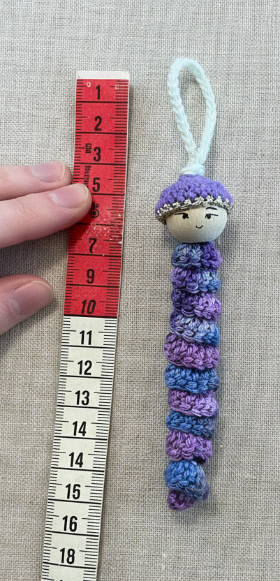 Handgemachtes Sorgenwürmchen in lila neben Lineal zur Größendarstellung ca 15 cm lang
