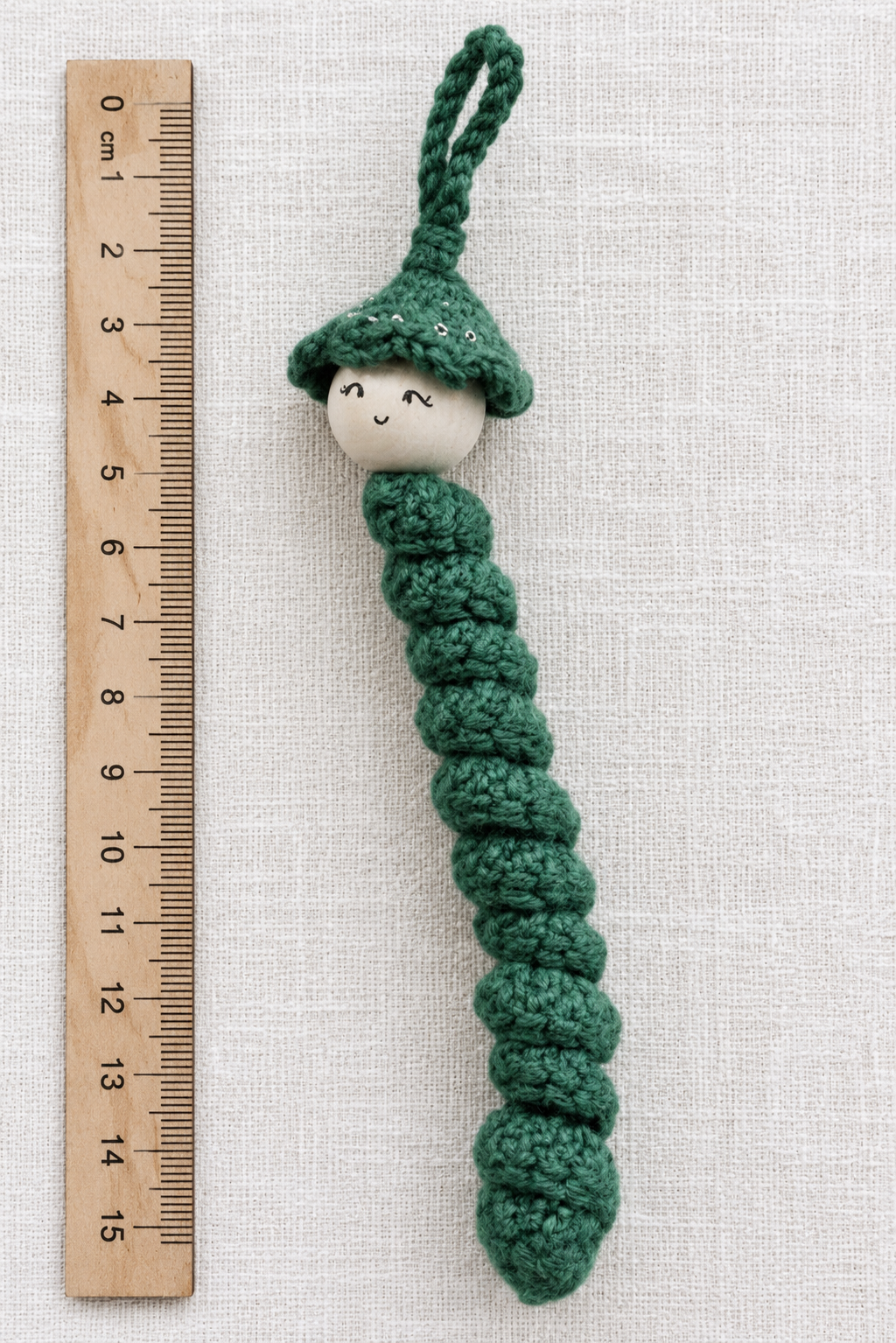 Grünes gehäkeltes Sorgenwürmchen mit Holzperle und Lineal zur Darstellung der Größe von ca. 13 cm.