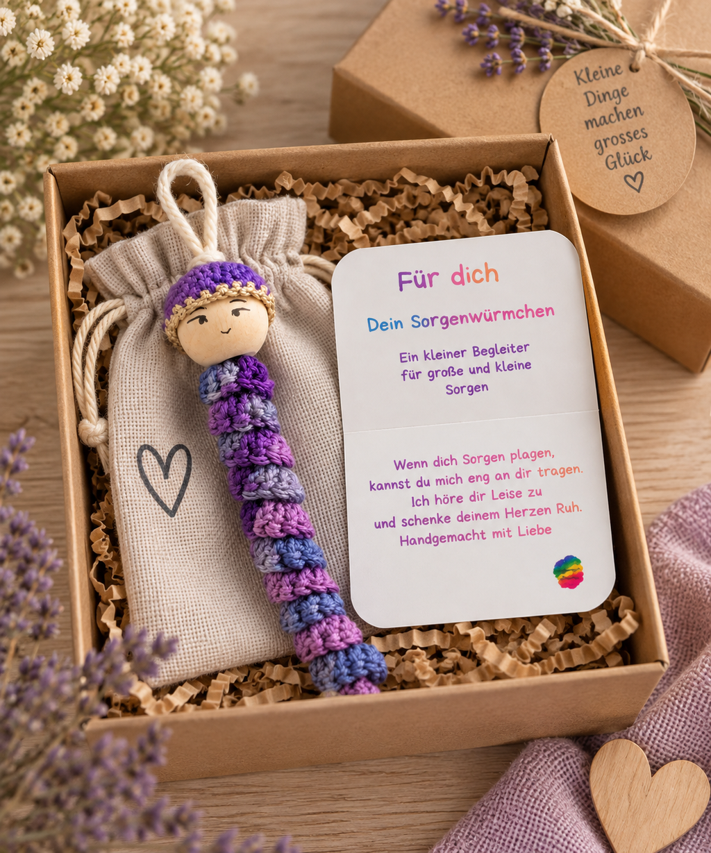 Lila gehäkeltes Sorgenwürmchen mit Kärtchen und Leinensäckchen liebevoll in einer Geschenkbox verpackt.