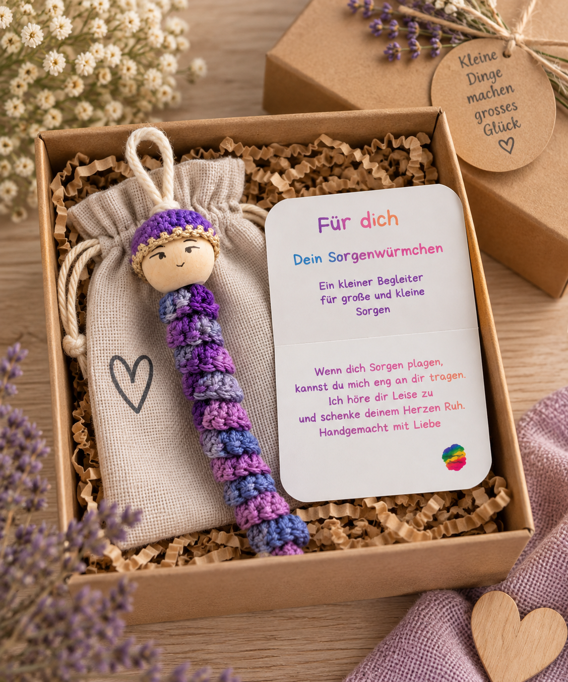 Lila gehäkeltes Sorgenwürmchen mit Kärtchen und Leinensäckchen liebevoll in einer Geschenkbox verpackt.