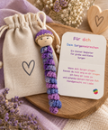 Lila gehäkeltes Sorgenwürmchen mit liebevollem Kärtchen und Leinensäckchen als handgemachte Geschenkidee.