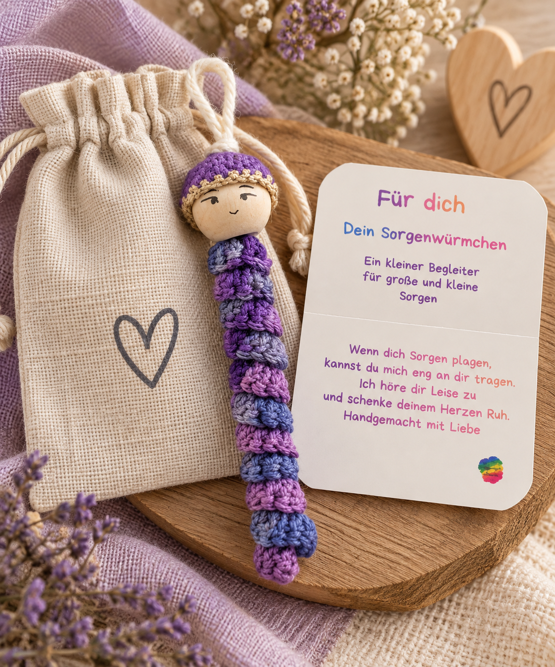 Lila gehäkeltes Sorgenwürmchen mit liebevollem Kärtchen und Leinensäckchen als handgemachte Geschenkidee.
